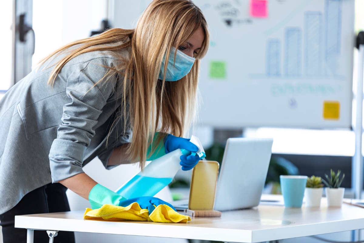 woman spraying office desk with cleaner and wiping with yellow cloth